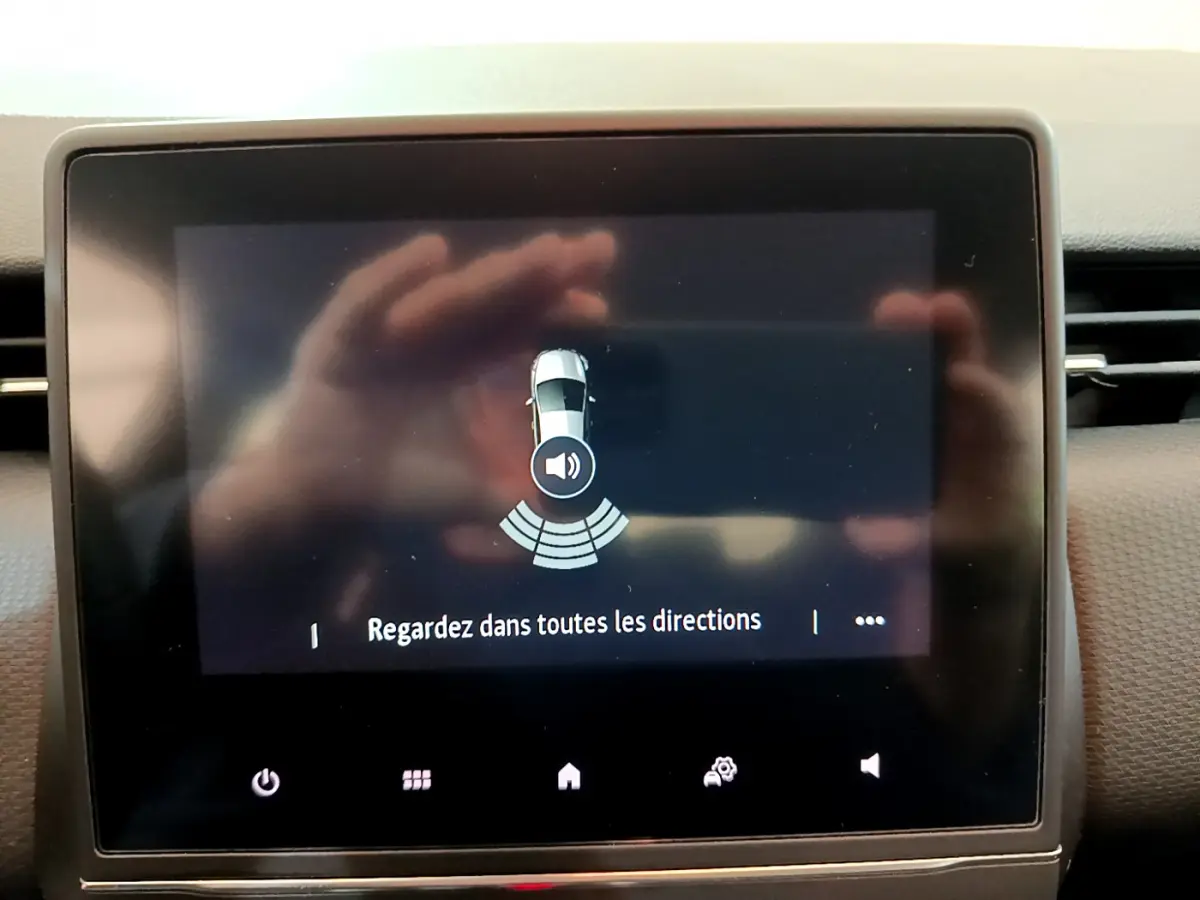 Écran tactile intérieur affichant l'alerte de capteurs de stationnement d'une Renault Clio blanche, vue de face.