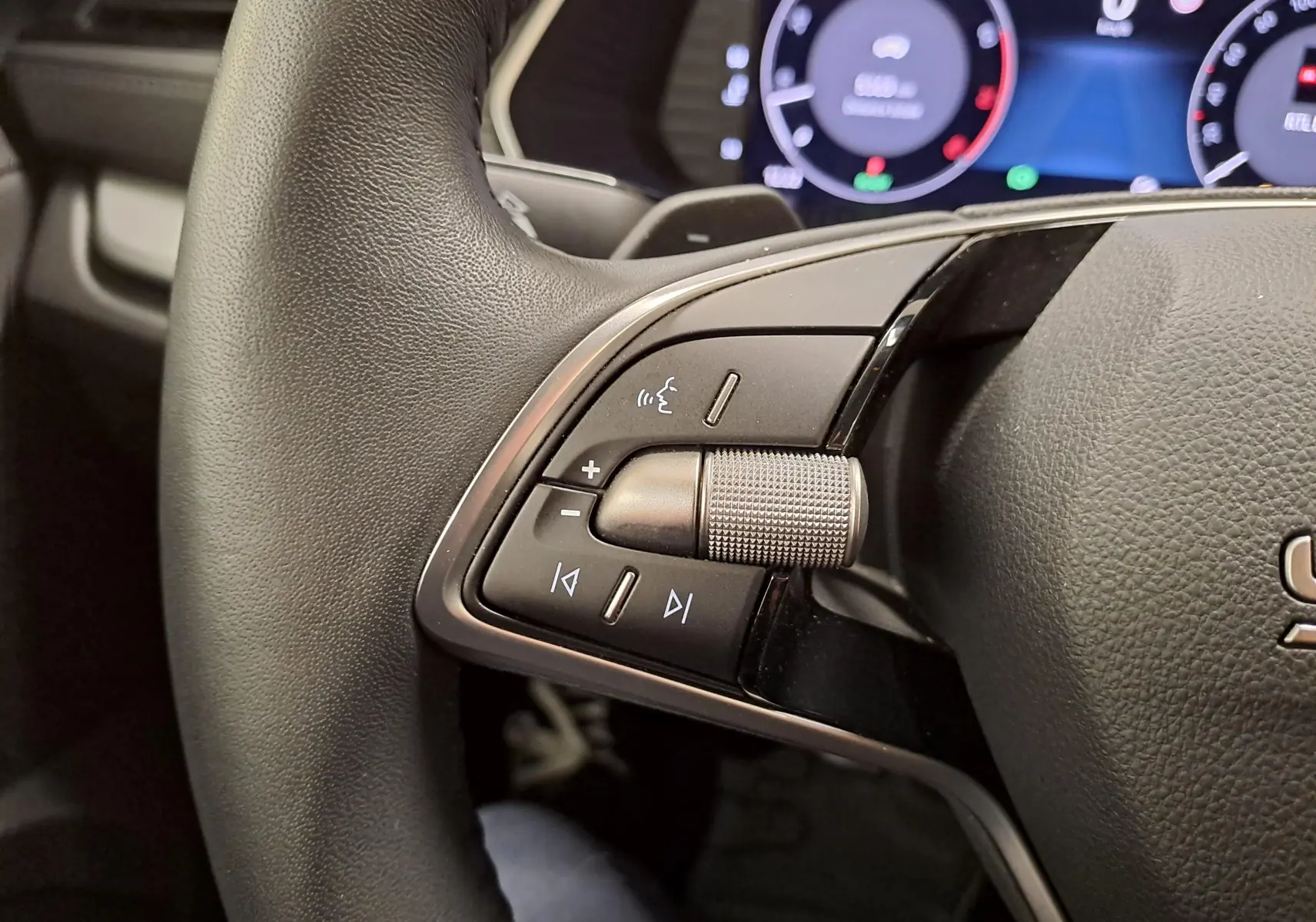 Gros plan sur les commandes gauche du volant du Skoda Octavia Combi 2025, avec tableau de bord numérique en arrière-plan.