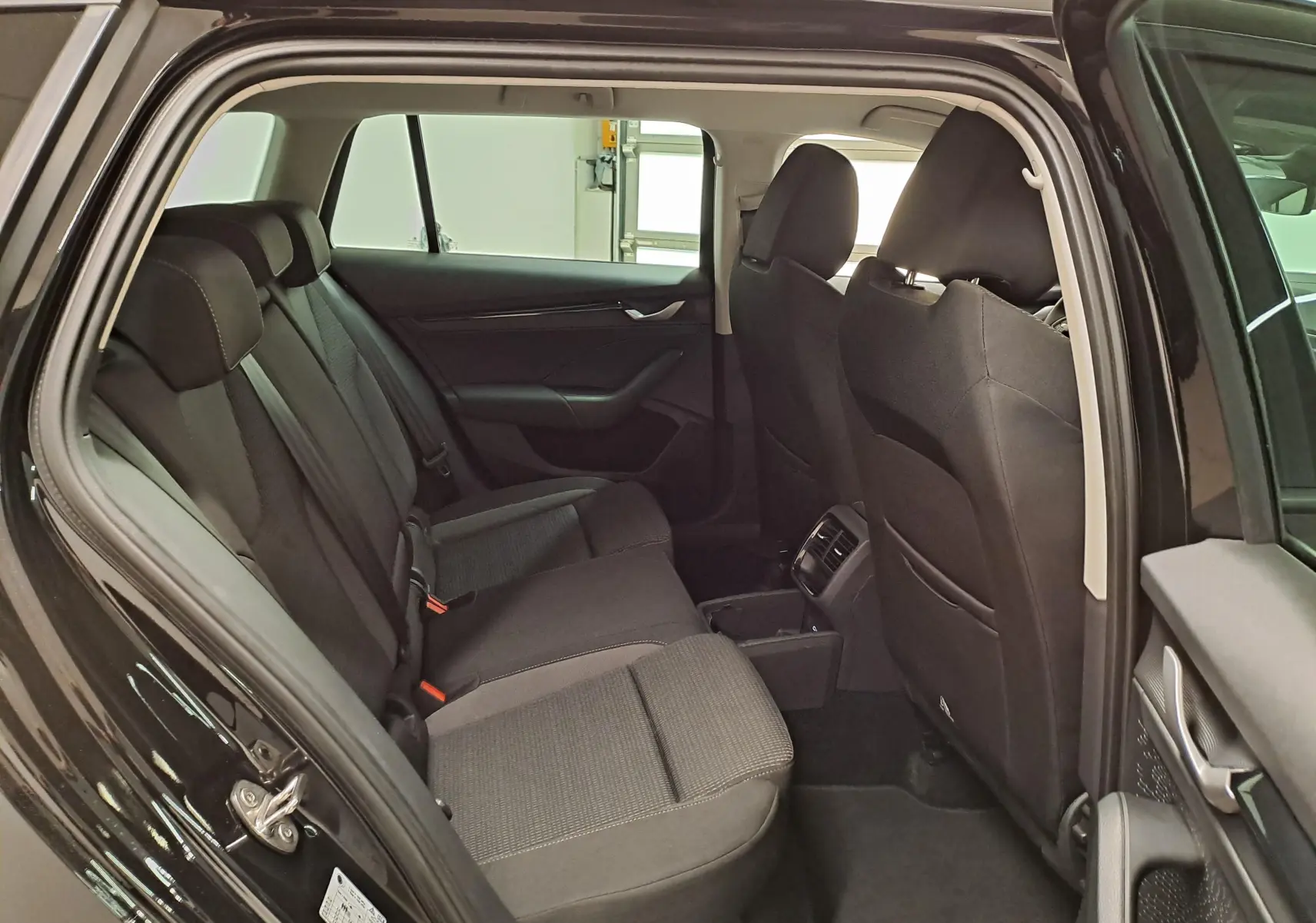 Vue intérieure côté gauche montrant les sièges arrière noirs et la porte ouverte d'une Skoda Octavia Combi 2025 Noir Magic nacré.