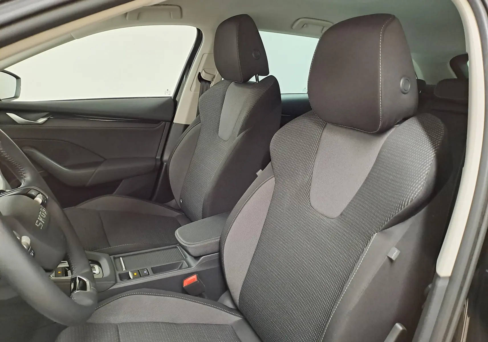Vue intérieure côté conducteur de la Skoda Octavia Combi 2025, sièges tissu noir avec console centrale et volant partiel visible.