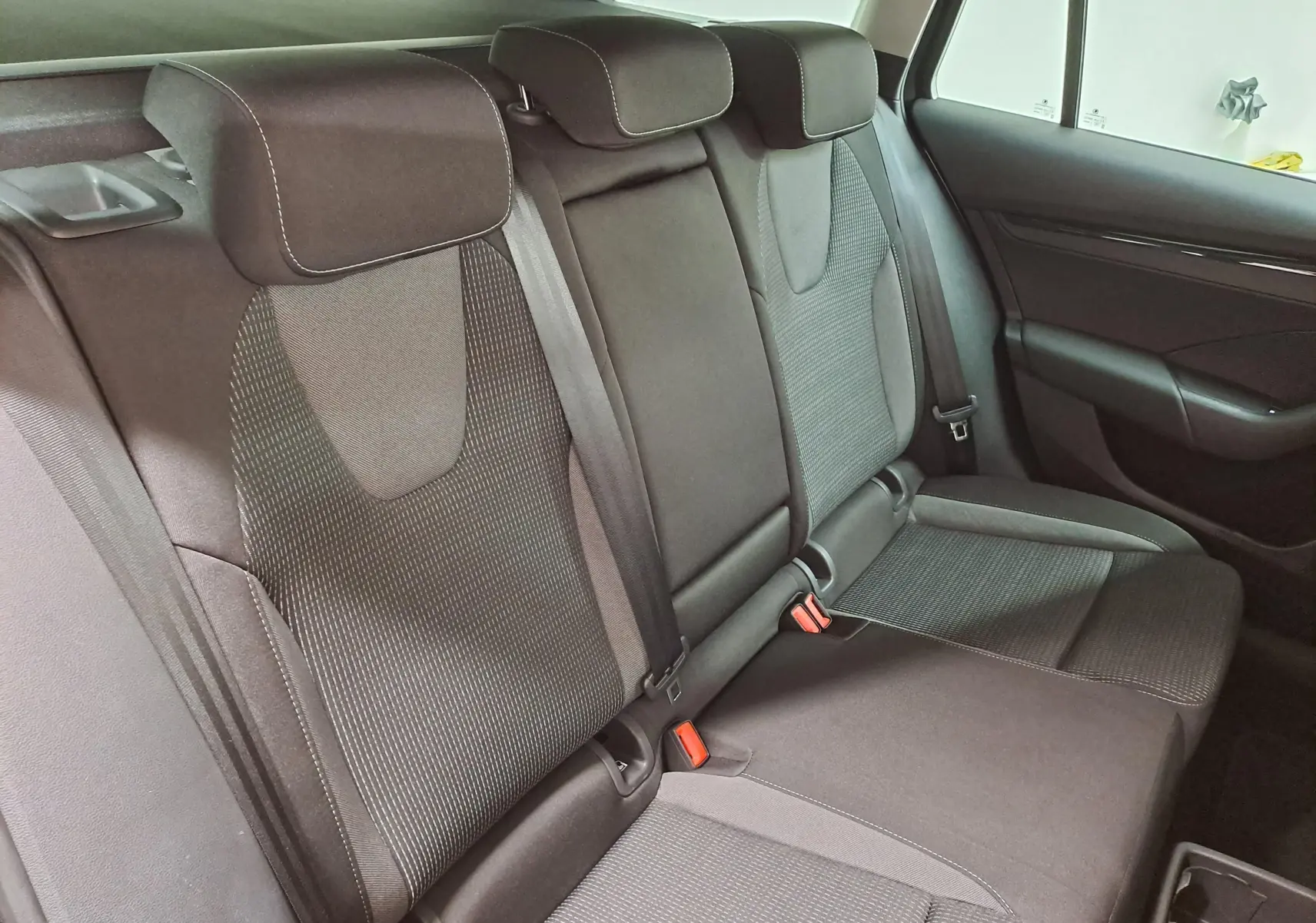 Vue intérieure sur les sièges arrière en tissu noir avec appuie-têtes et ceintures de sécurité visibles.