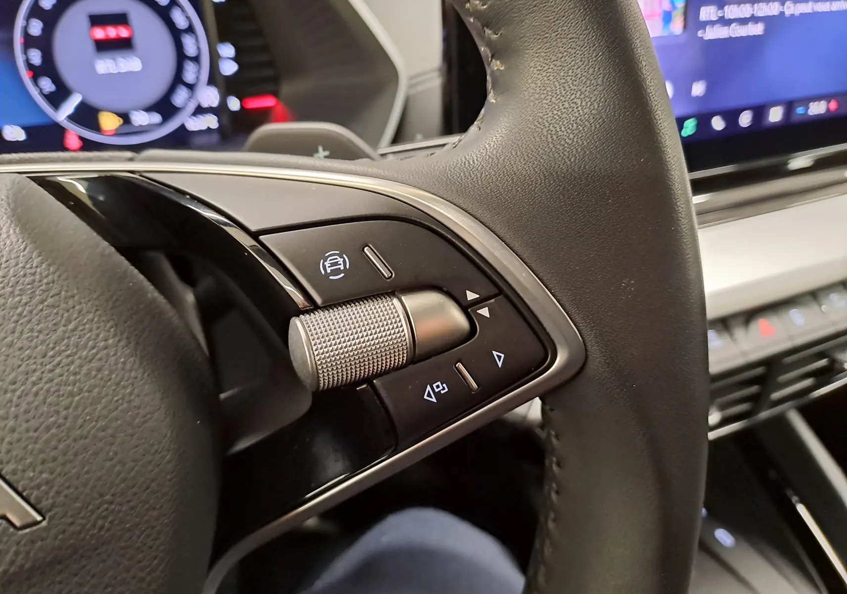 Gros plan sur les commandes au volant à droite du Skoda Octavia Combi noir Magic nacré, avec tableau de bord numérique en arrière-plan.