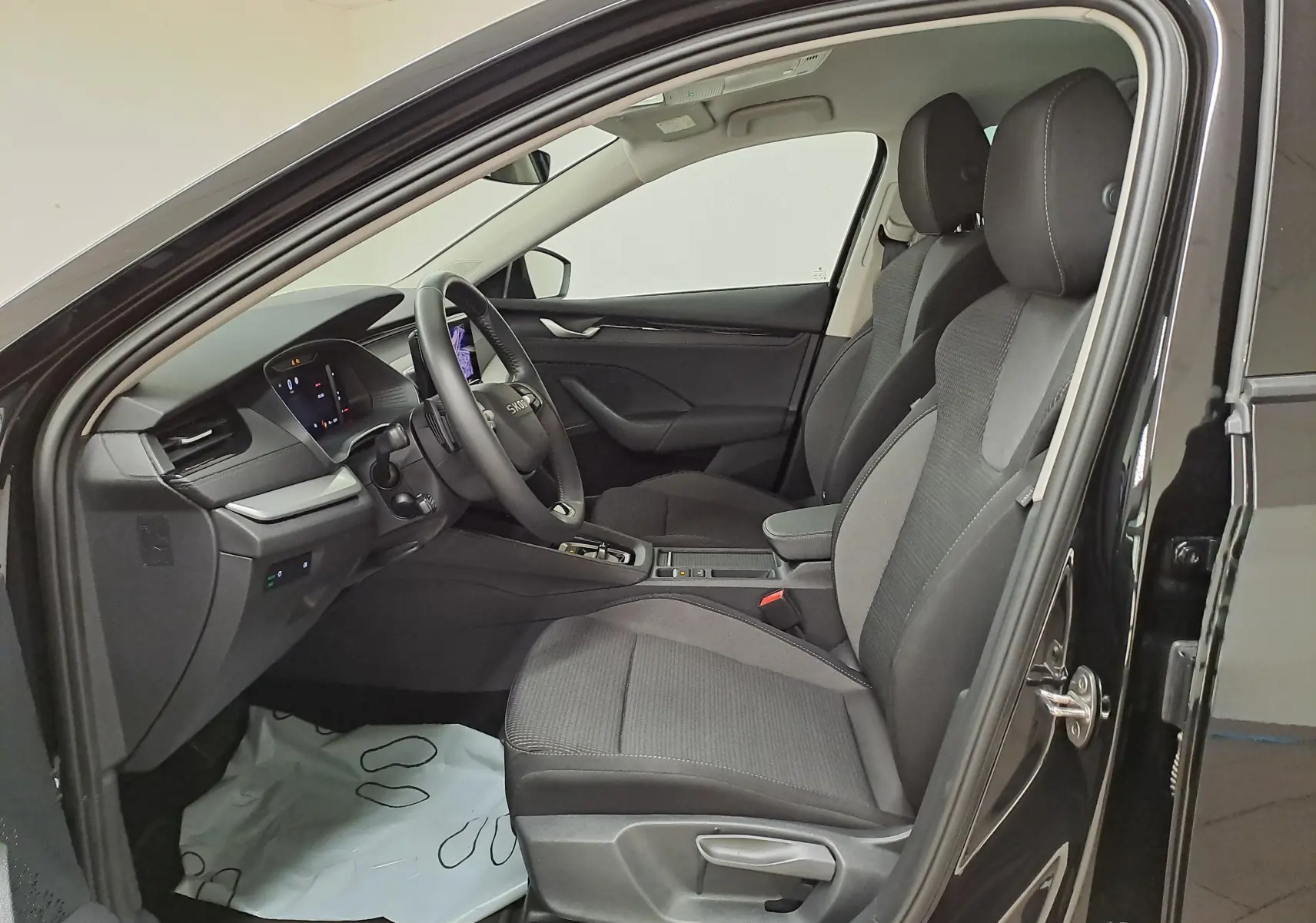 Vue intérieure côté conducteur de la Skoda Octavia Combi 2025 noir Magic avec sièges tissu et tableau de bord moderne.