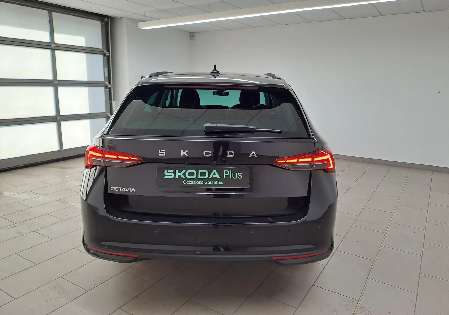 Vue arrière d'une Skoda Octavia Combi 2025 noire Magic nacré avec feux LED allumés dans un garage lumineux.