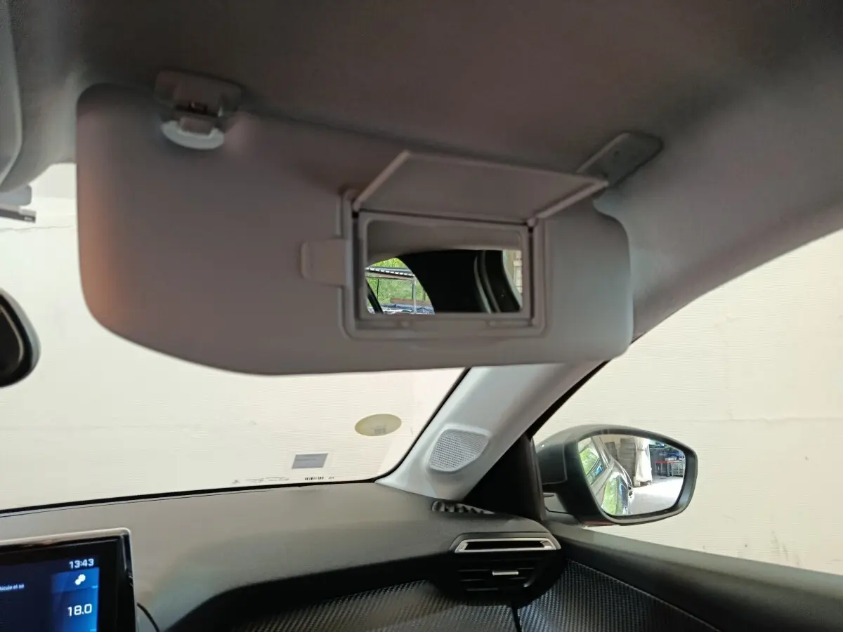 Intérieur de la Peugeot 208 BlueHDi 100, vue côté passager avec pare-soleil et miroir éclairé ouvert.