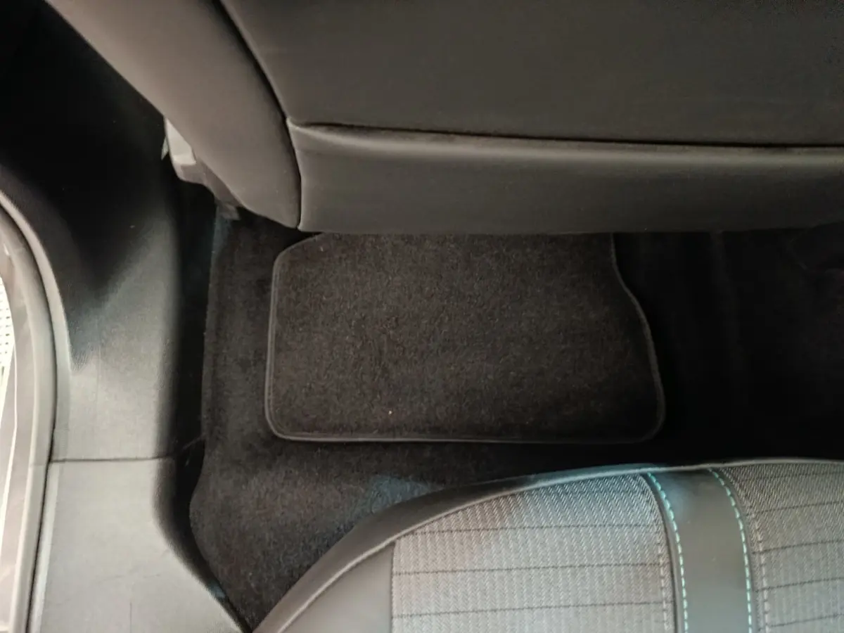 Vue intérieure du plancher arrière côté droit d'une Peugeot 208 2020 avec tapis de sol noir et siège tissu gris à surpiqûres bleues.