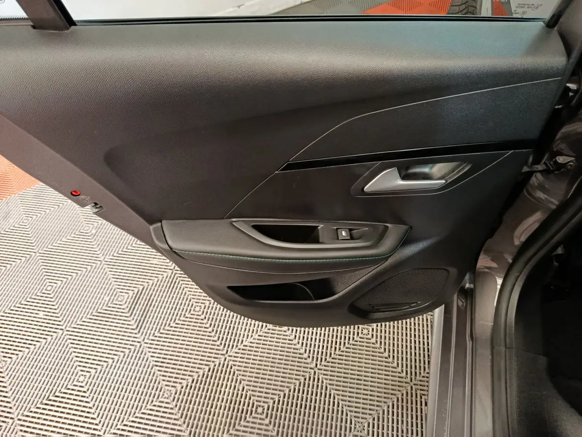 Vue latérale du panneau de porte arrière gauche noir avec poignée argentée et commande de fenêtre sur Peugeot 208.