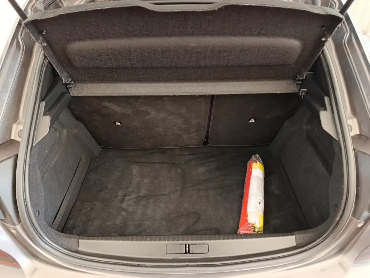 Coffre ouvert vu de dessus d’une Peugeot 208 2020, moquette noire avec triangle de signalisation rangé à droite.