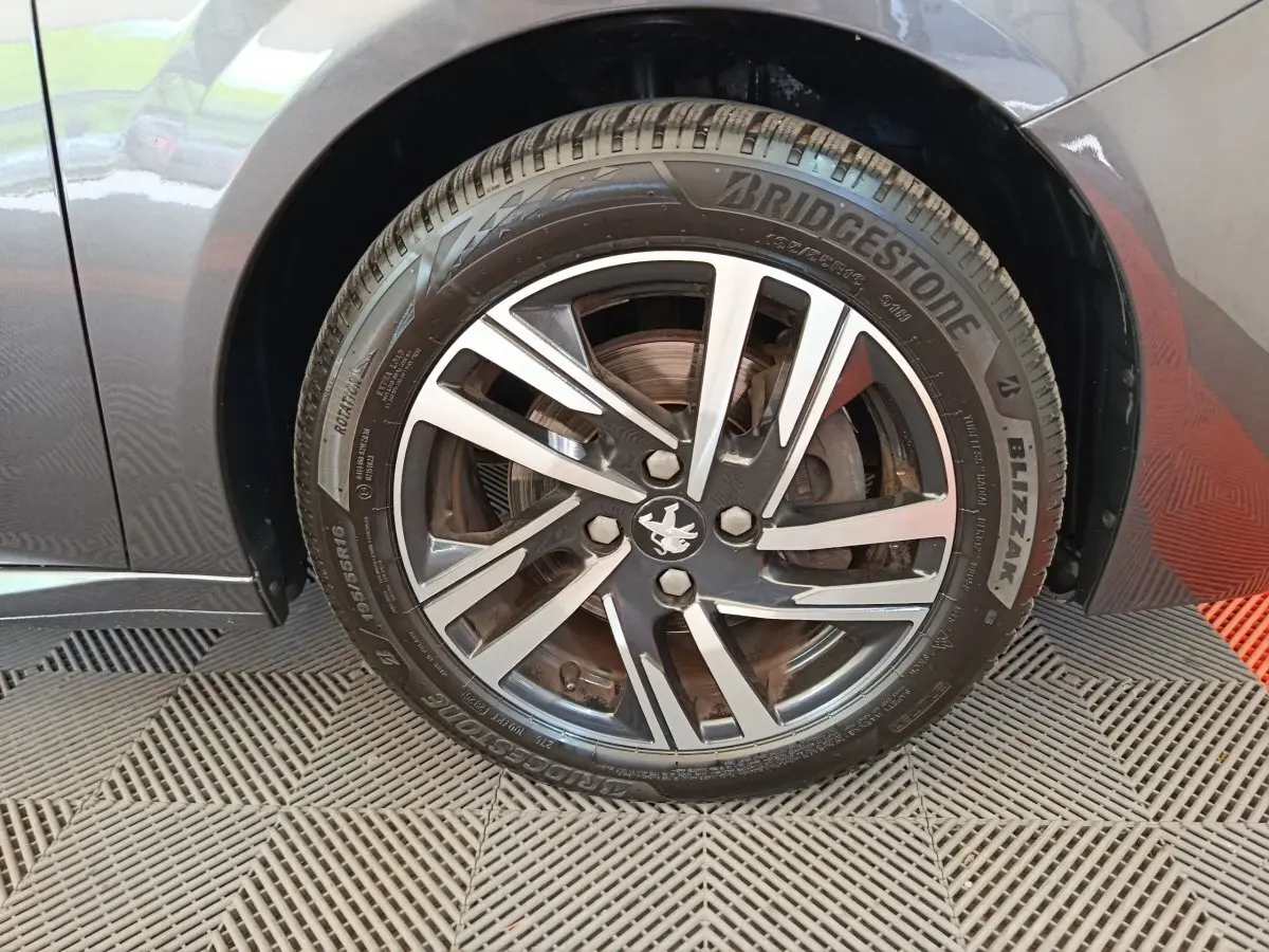 Gros plan sur la roue avant gauche grise d'une Peugeot 208 avec jante alliage et pneu Bridgestone Blizzak.