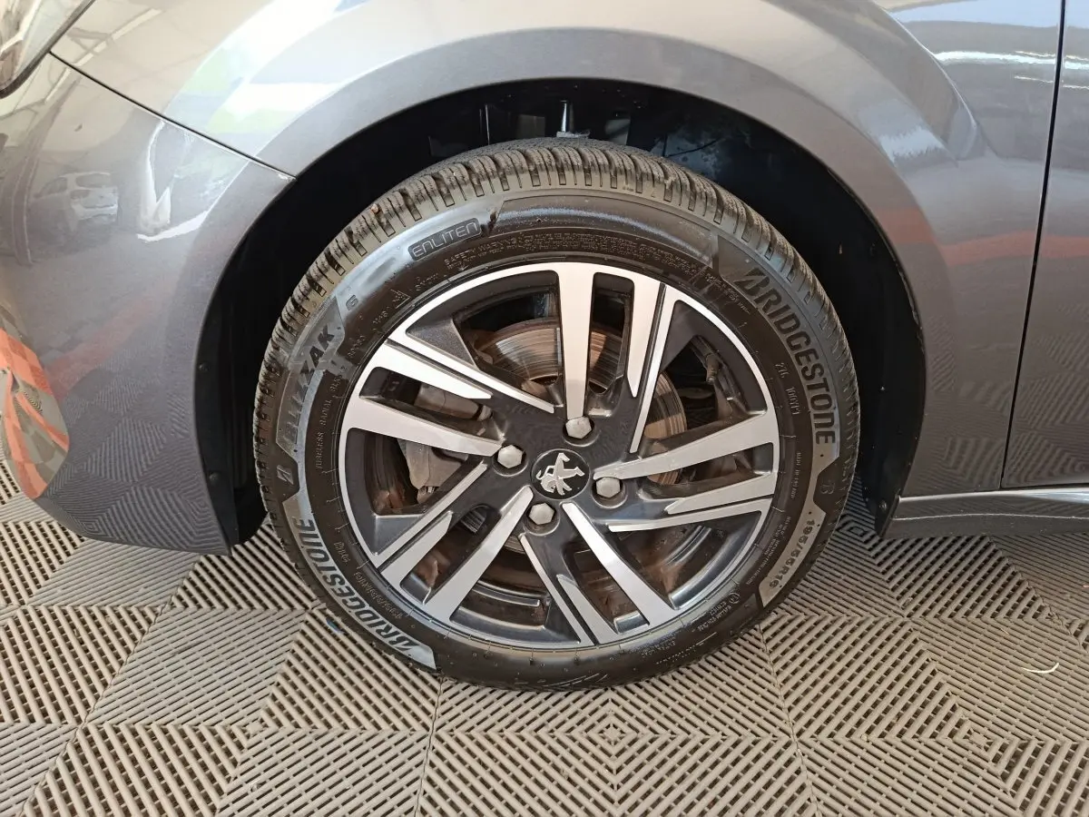 Gros plan sur la roue avant gauche grise d'une Peugeot 208 avec jante alliage et logo lion central.