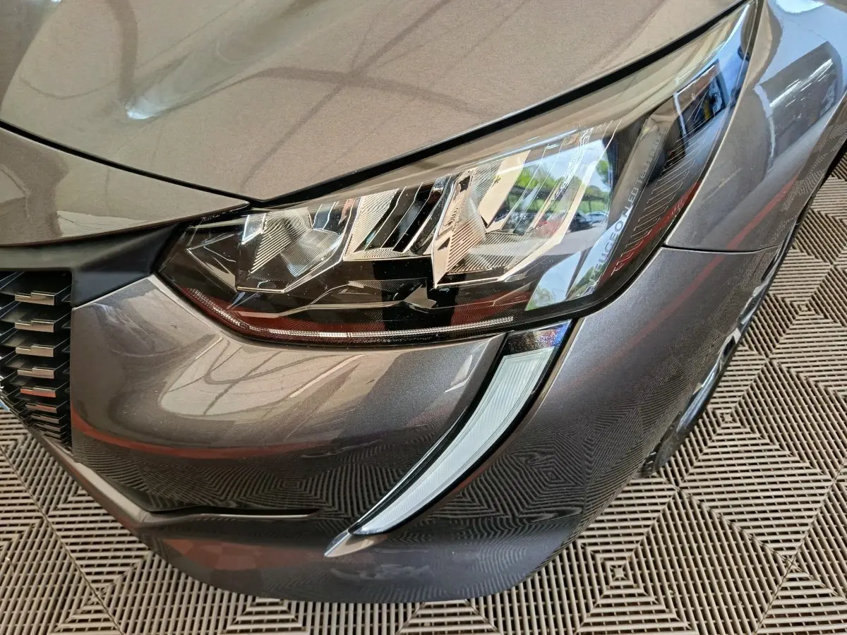 Gros plan sur le phare avant droit gris métallisé d'une Peugeot 208 avec signature lumineuse LED distinctive.