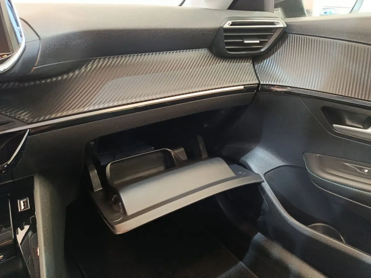 Intérieur côté passager de la Peugeot 208 2020 avec boîte à gants ouverte et tableau de bord noir à effet carbone.
