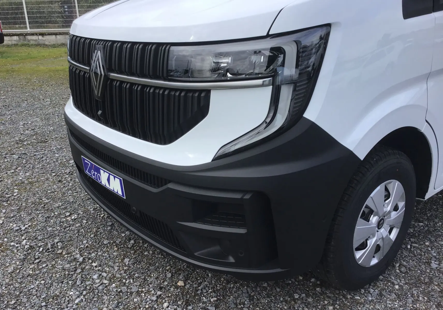 Gros plan sur l’avant droit du Renault Master blanc 2026 avec calandre noire et phare moderne, sur sol gravillonné.