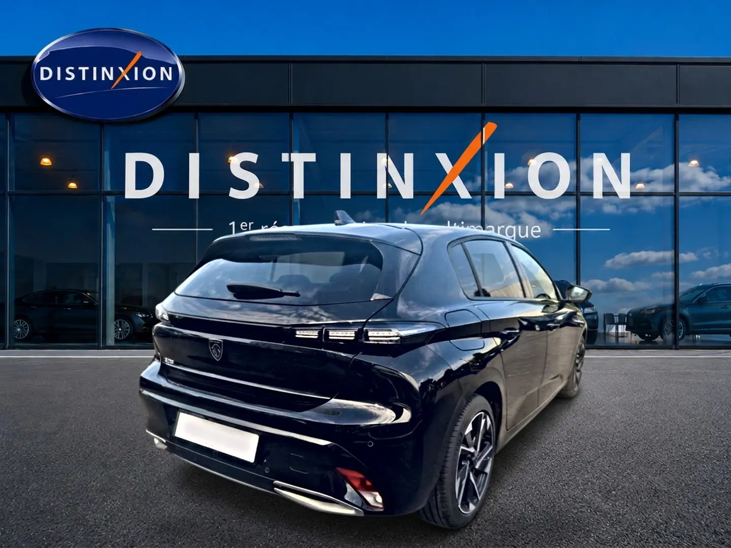 Vue 3/4 arrière droite d'une Peugeot 308 noire 2025 avec feux arrière LED et jantes alliage devant un bâtiment vitré Distinxion.