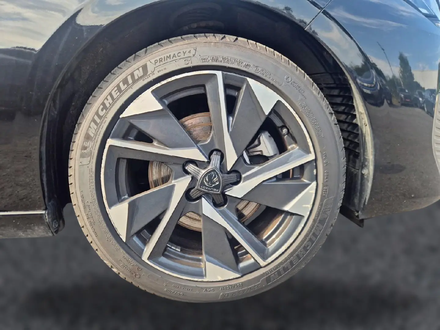 Gros plan sur la jante alu noire et grise de la roue avant droite d'une Peugeot 308 noire 2025.