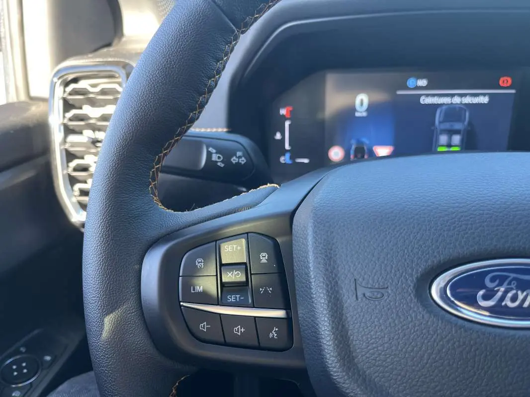 Gros plan sur le volant en cuir noir du Ford Ranger 2026, avec commandes multifonctions et tableau de bord numérique en arrière-plan.