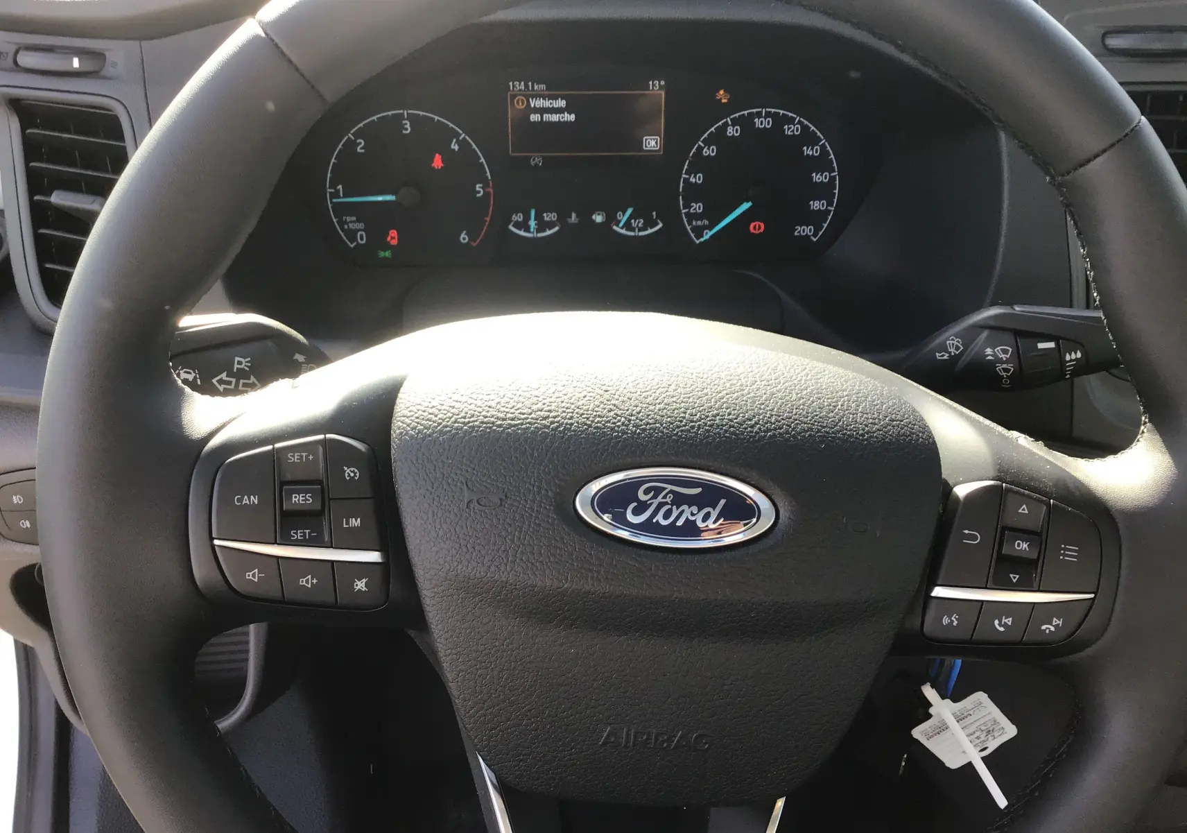 Vue rapprochée du volant Ford avec commandes intégrées et tableau de bord numérique du Transit Chassis Cabine blanc.
