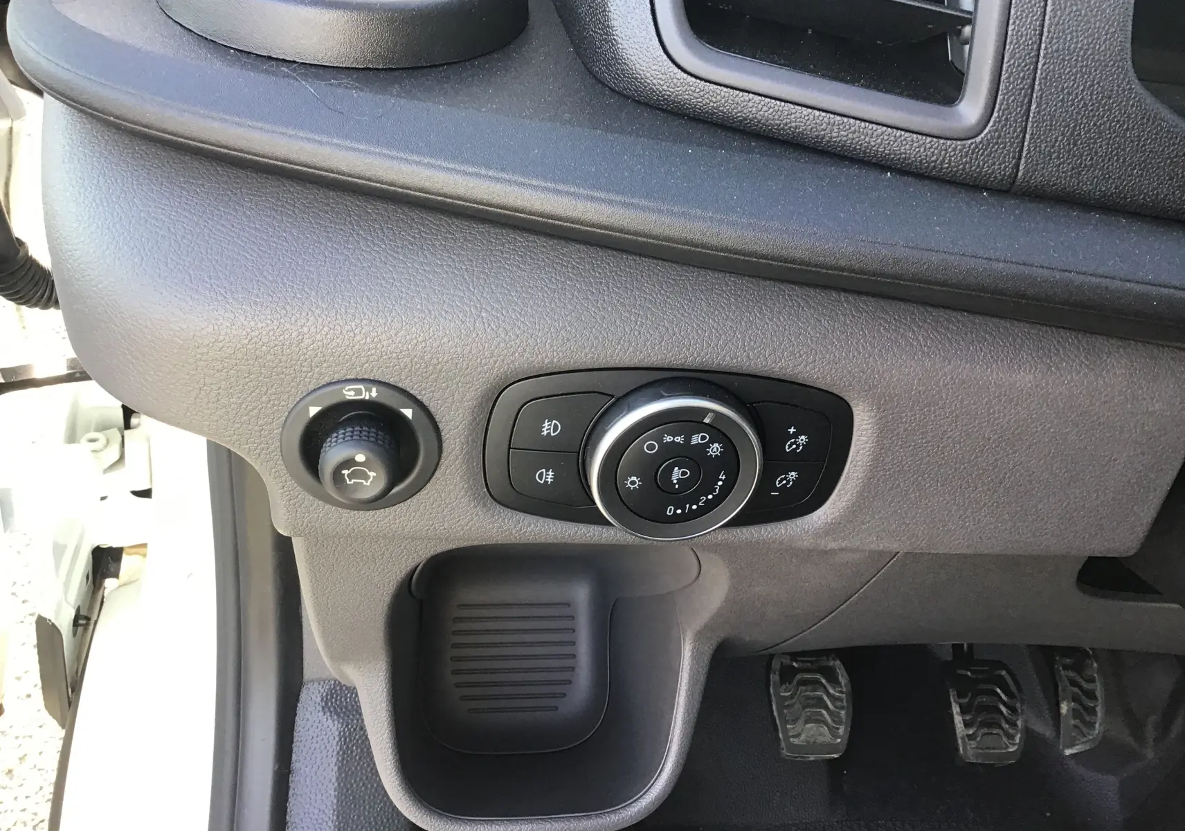 Vue intérieure côté conducteur du tableau de bord gris du Ford Transit Châssis Cabine avec commandes d'éclairage et pédales manuelles visibles.