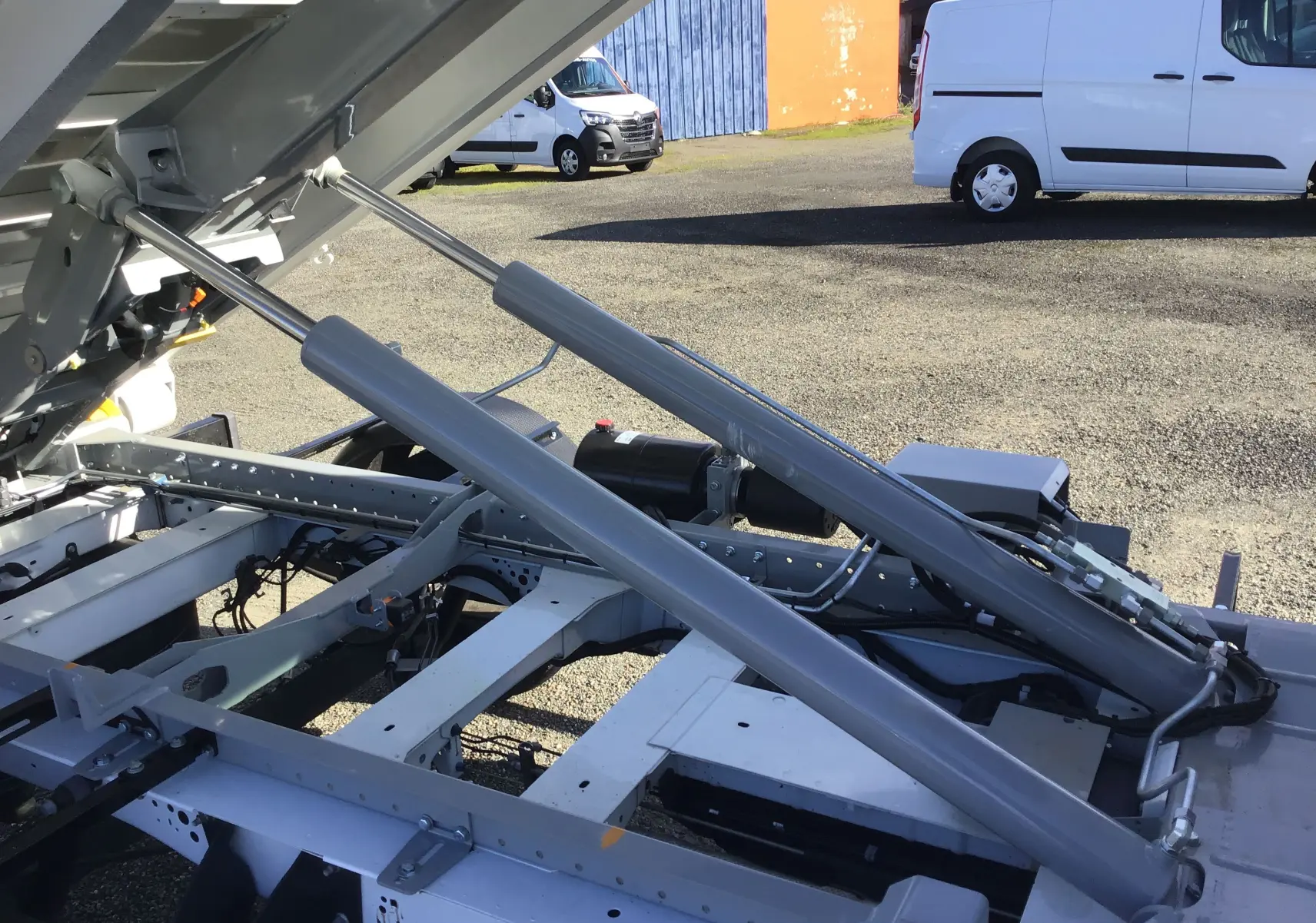 Détail du bras polybenne relevé sur le châssis blanc du Ford Transit L2 T350, vu de côté extérieur.