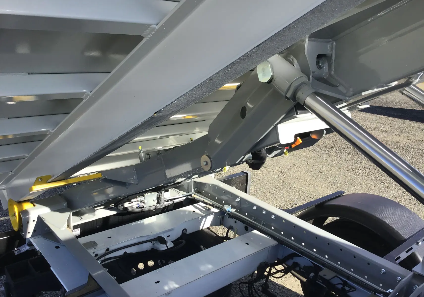 Gros plan sous la benne relevée d'un Ford Transit Châssis Cabine blanc, montrant le bras polybenne et la structure métallique.