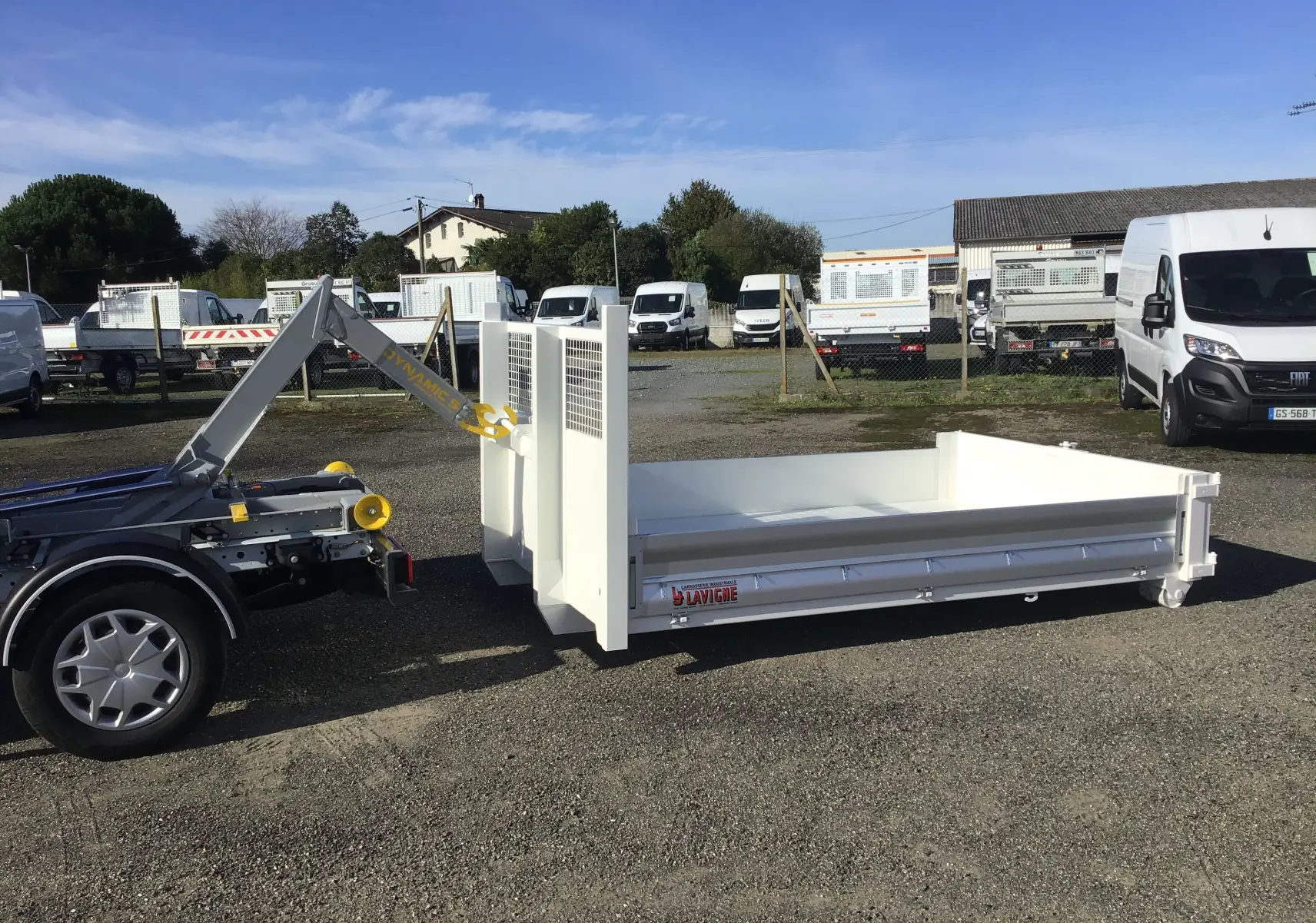 Vue latérale droite du châssis cabine Ford Transit blanc avec bras polybenne et benne 3m20 posée au sol.