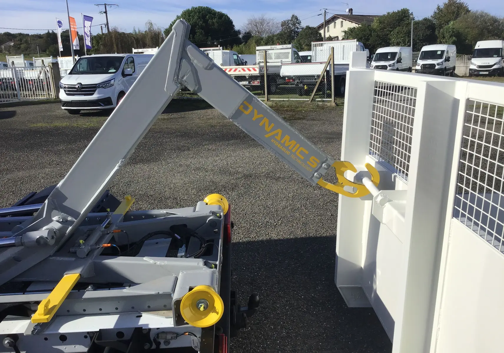 Gros plan sur le bras polybenne gris et jaune du Ford Transit Chassis cabine blanc, vu de l'arrière côté droit.