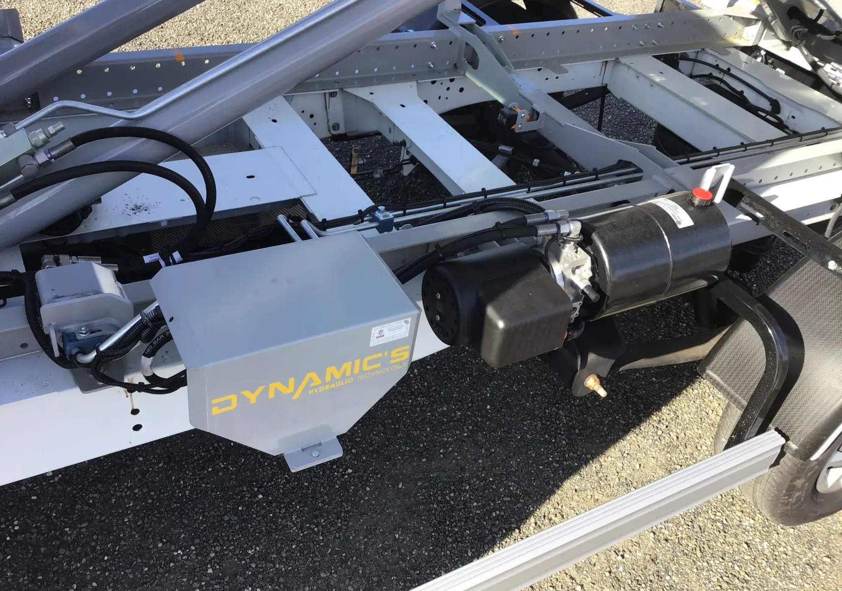 Gros plan sur le bras polybenne hydraulique gris et noir du châssis cabine blanc du Ford Transit côté droit.