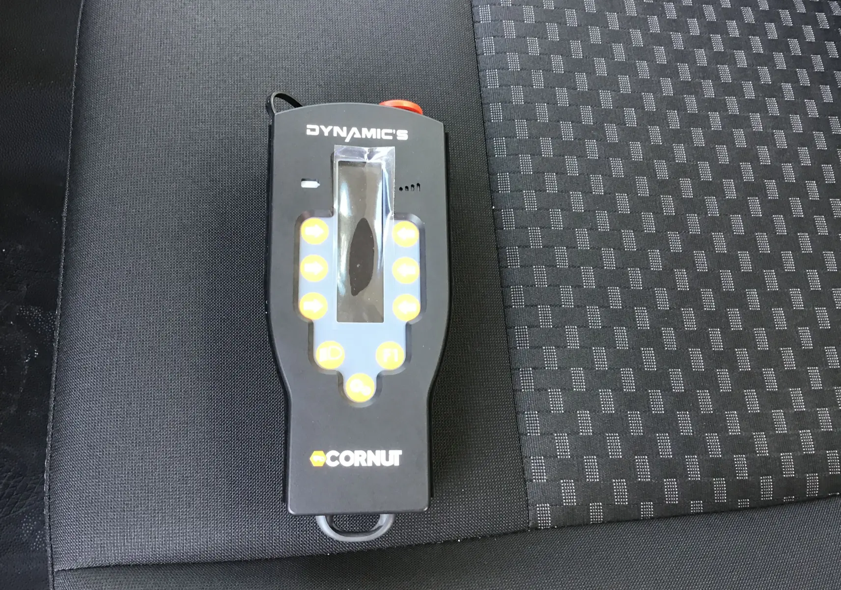 Télécommande noire Dynamic's Cornut posée sur un siège tissu gris foncé à motifs carrés dans un Ford Transit Chassis Cabine blanc.