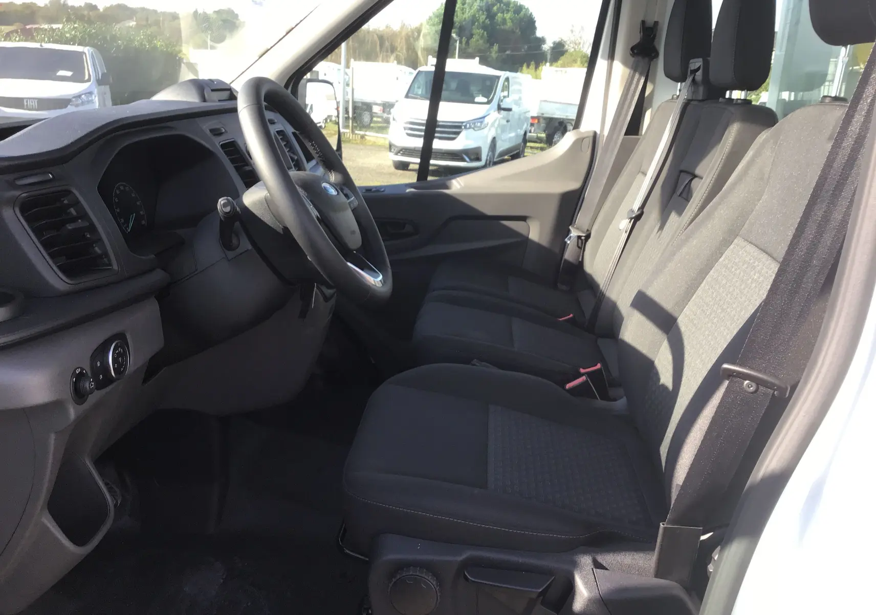 Intérieur du Ford Transit Chassis Cabine blanc, vue côté conducteur montrant les sièges noirs et le tableau de bord moderne.