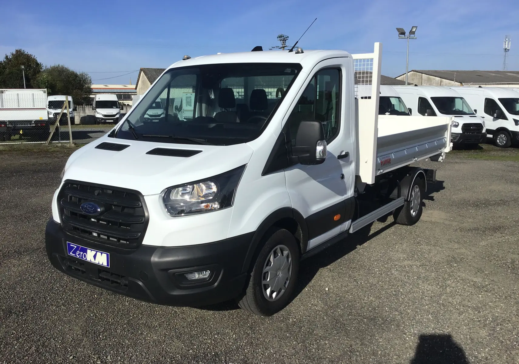 Ford Transit Chassis Cabine blanc vu en 3/4 avant droit avec benne et bras polybenne sur parking extérieur.