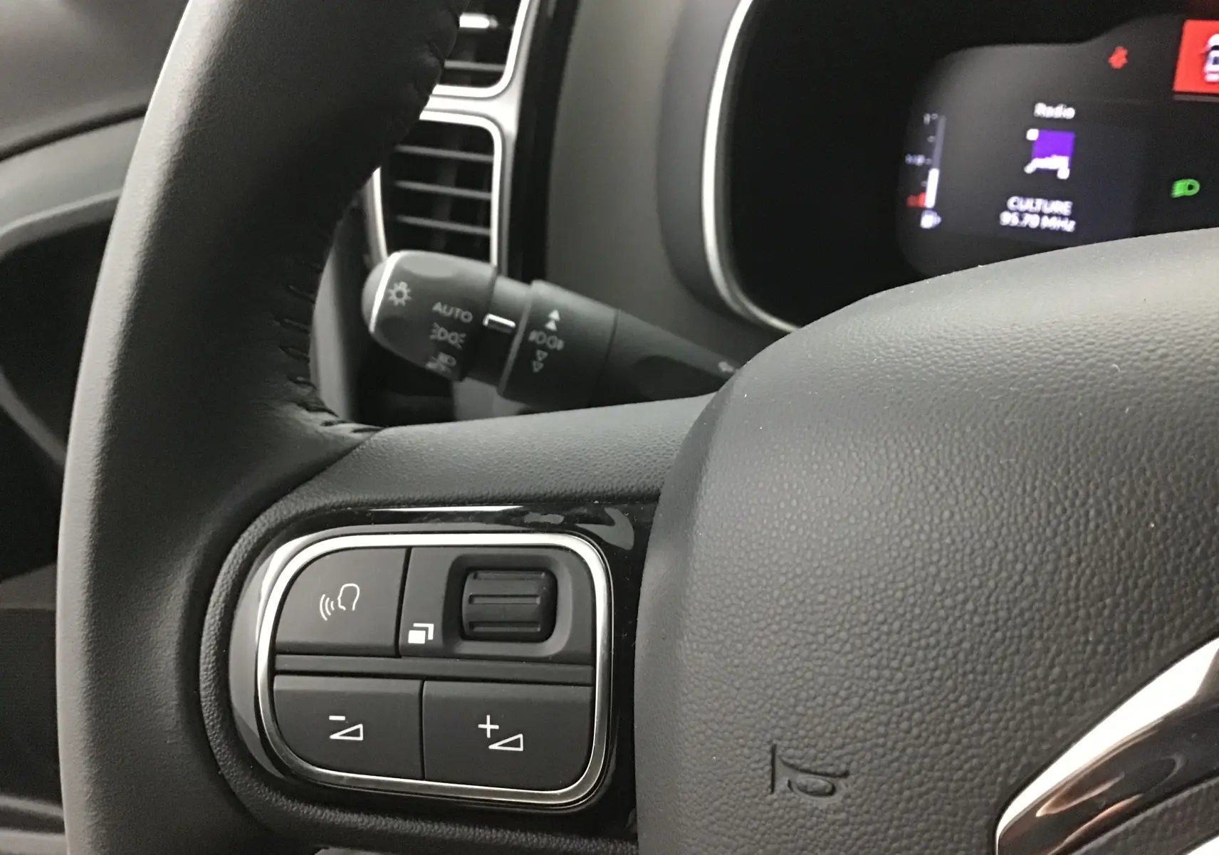 Gros plan sur les commandes du volant cuir noir d'un Citroën C5 Aircross gris Artense, avec tableau de bord numérique en arrière-plan.