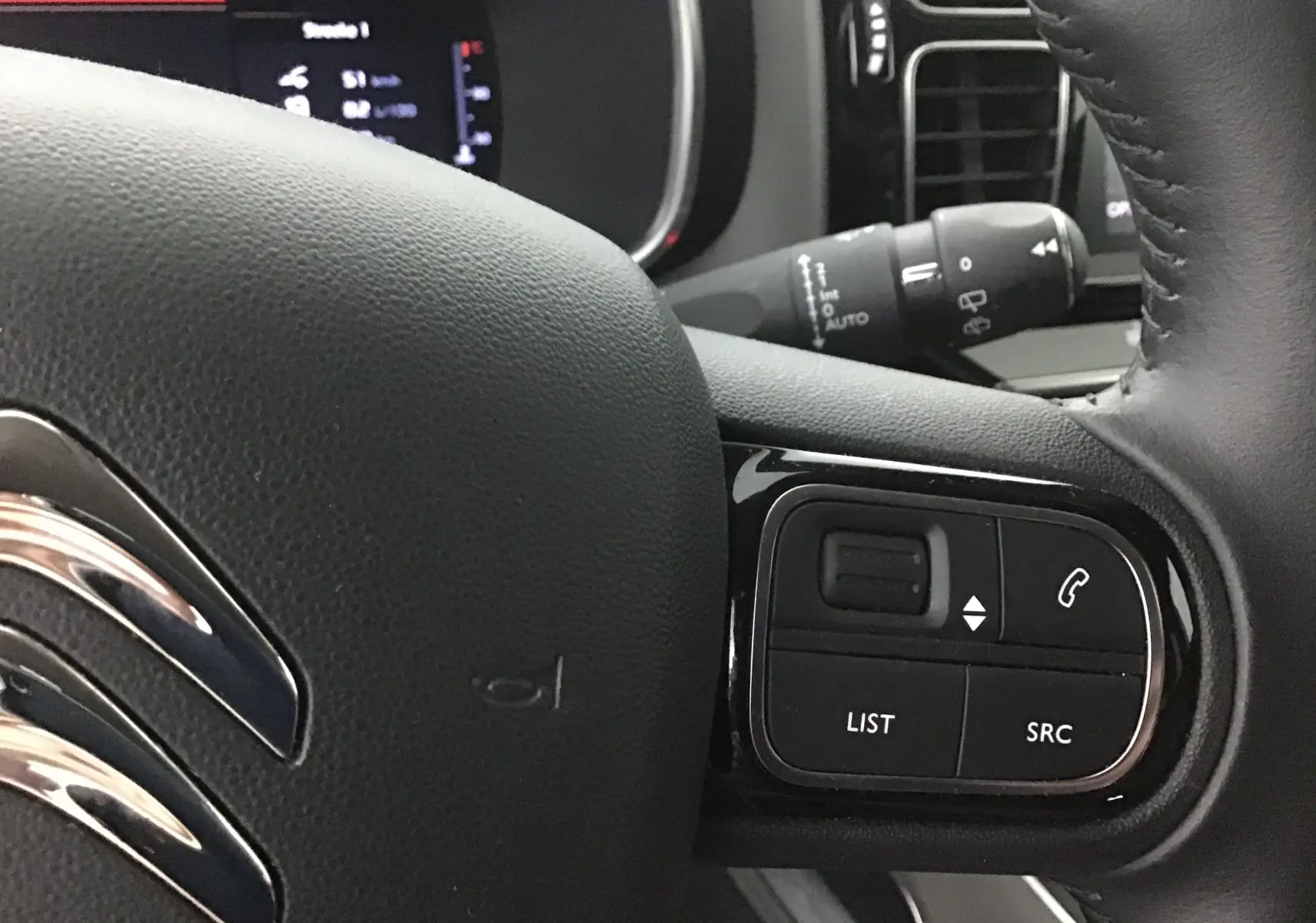 Gros plan sur le volant en cuir noir du Citroën C5 Aircross gris, avec commandes audio et téléphone intégrées.