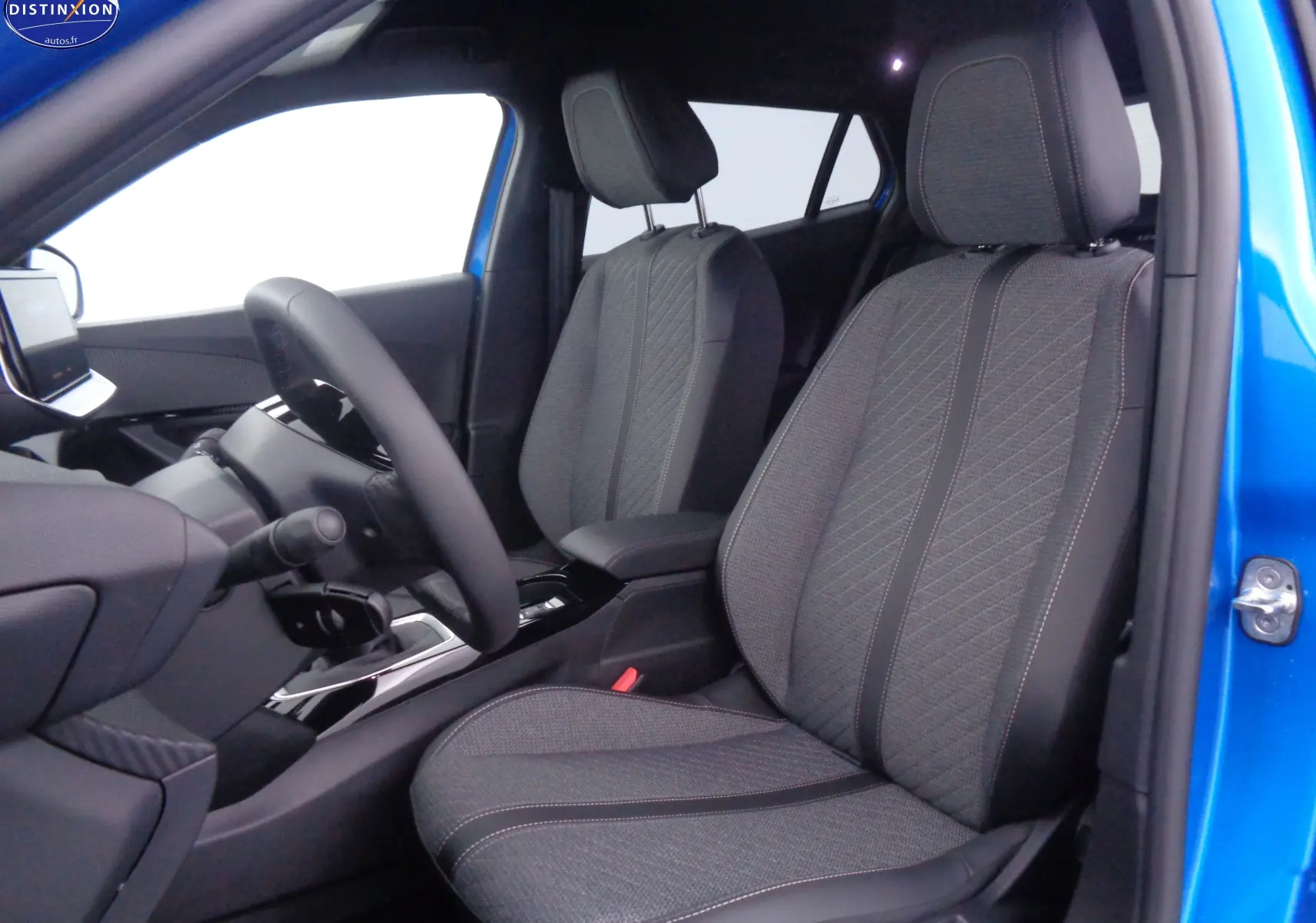 Vue intérieure côté conducteur du Peugeot 2008 bleu Vertigo, sièges avant en tissu gris avec surpiqûres contrastantes.