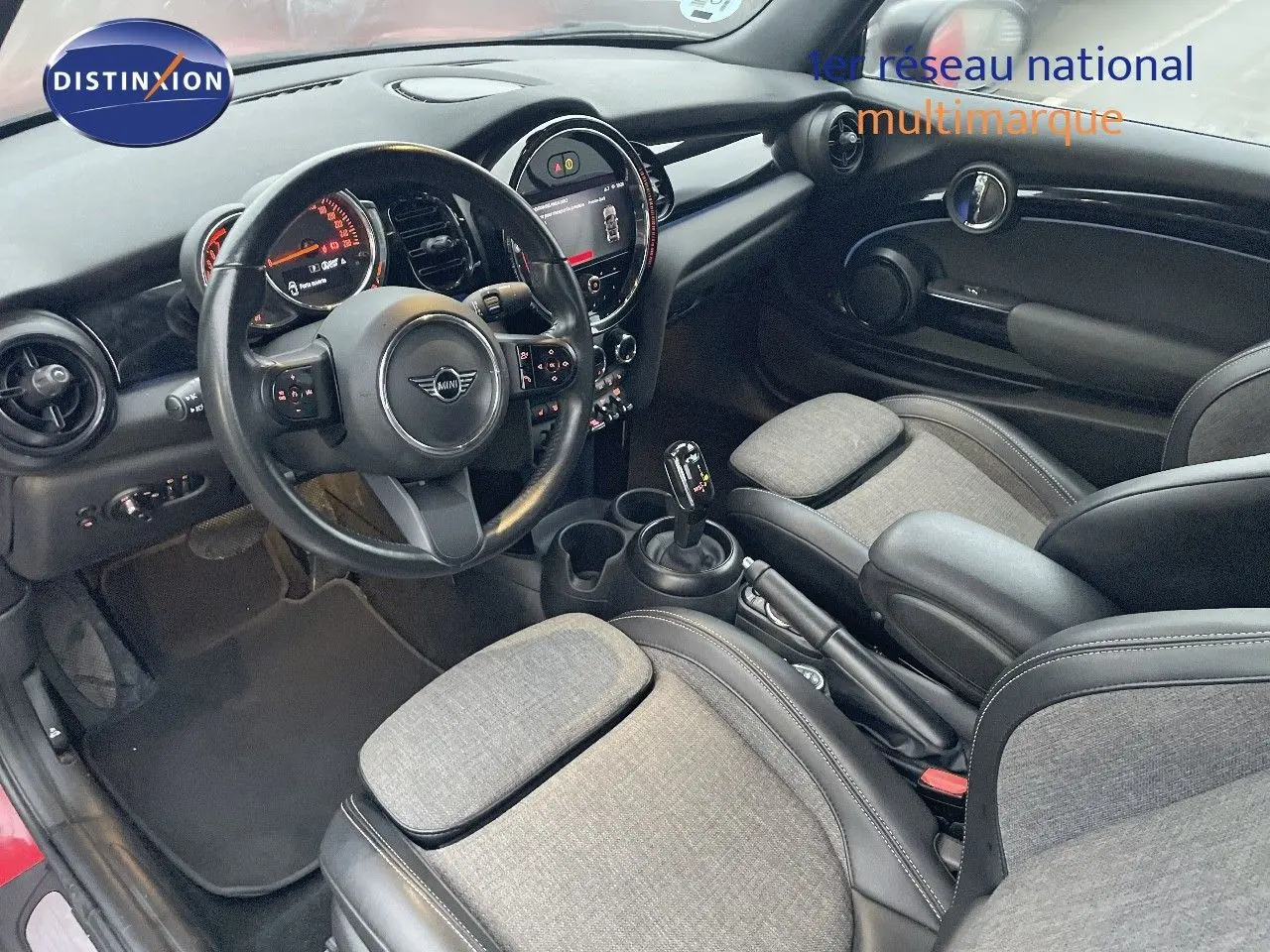 Vue intérieure côté conducteur de la MINI Cabriolet rouge chili 2023, avec tableau de bord moderne et sièges tissu-cuir gris.