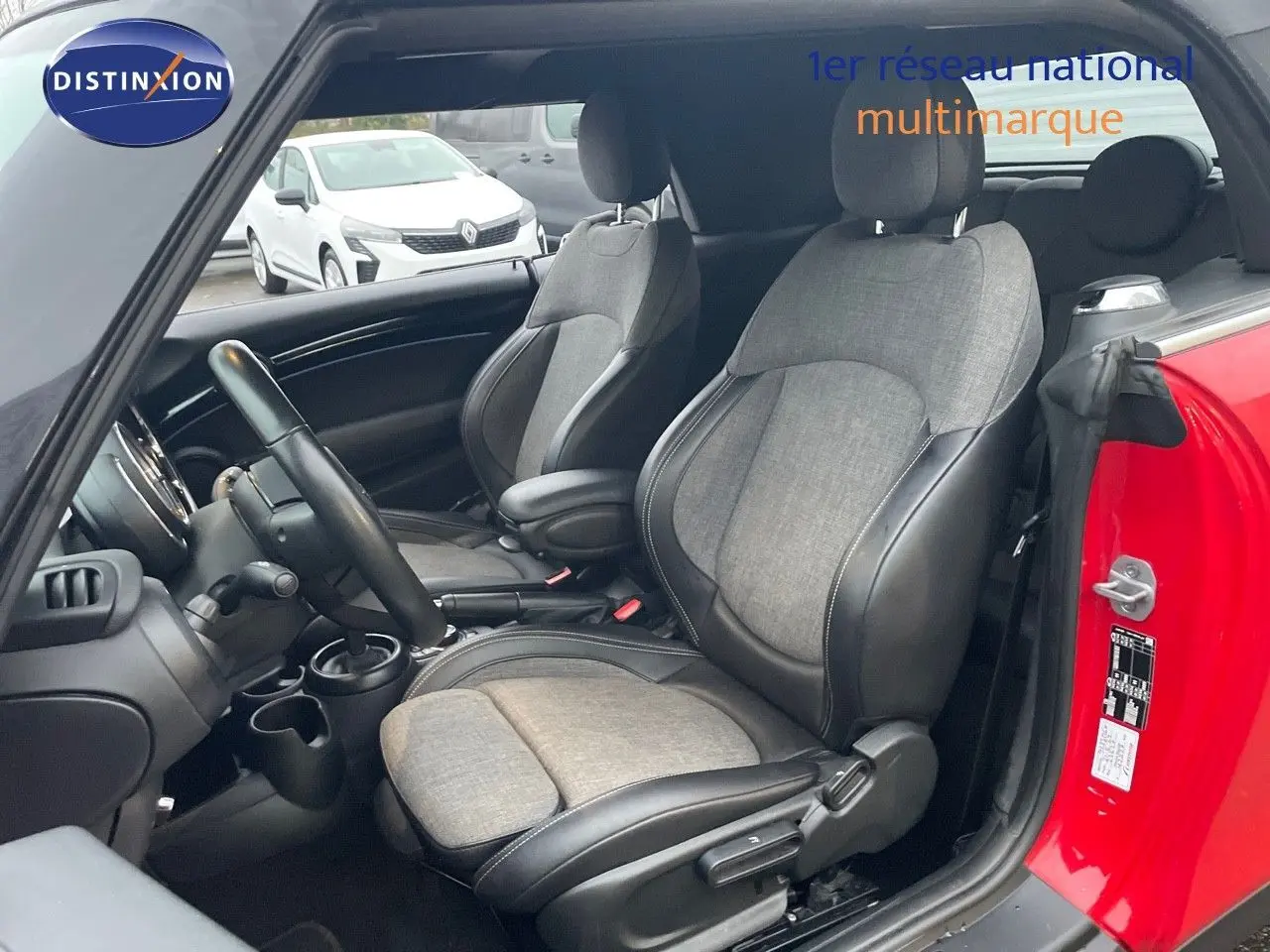 Vue intérieure côté conducteur d'une MINI Cabriolet F57 rouge chili, sièges tissu gris et cuir noir, volant et tableau de bord visibles.