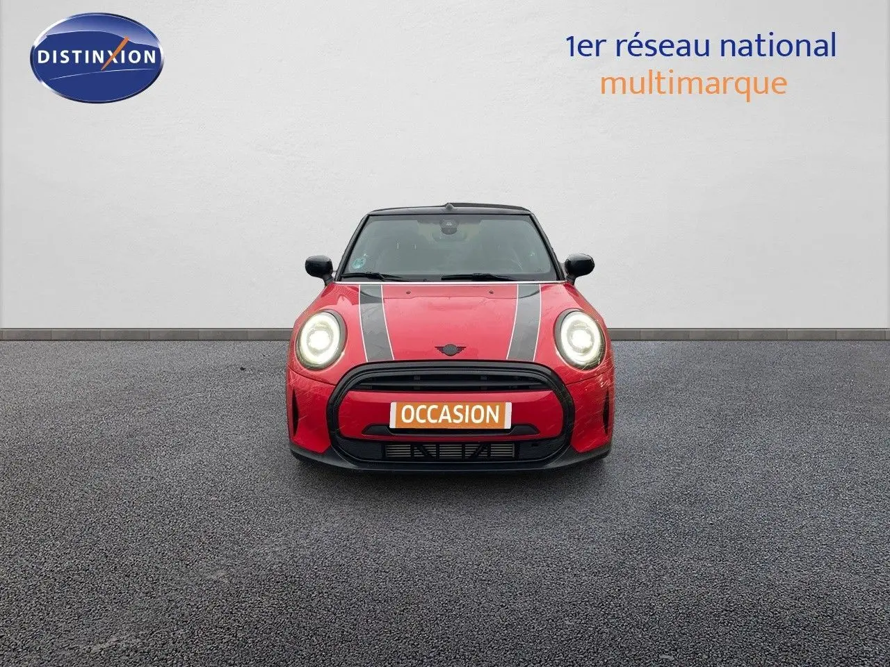Vue frontale d'une MINI Cabriolet F57 rouge chili avec bandes noires et phares allumés sur fond neutre.