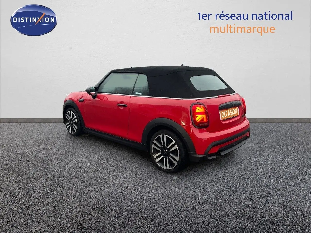Vue 3/4 arrière droite d'une MINI Cabriolet rouge chili avec toit noir fermé et jantes bi-ton sur sol gris.