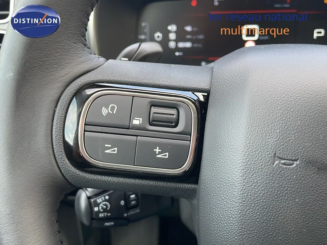 Gros plan sur les commandes au volant noir du Citroën C5 Aircross 2025 blanc, avec tableau de bord numérique en arrière-plan.