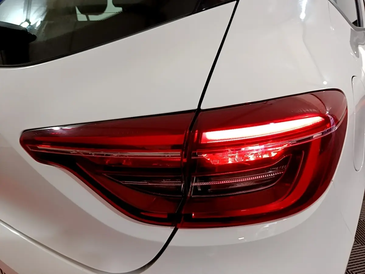 Gros plan sur le feu arrière droit rouge allumé d’une Renault Clio Business blanche, vue de trois quarts arrière.