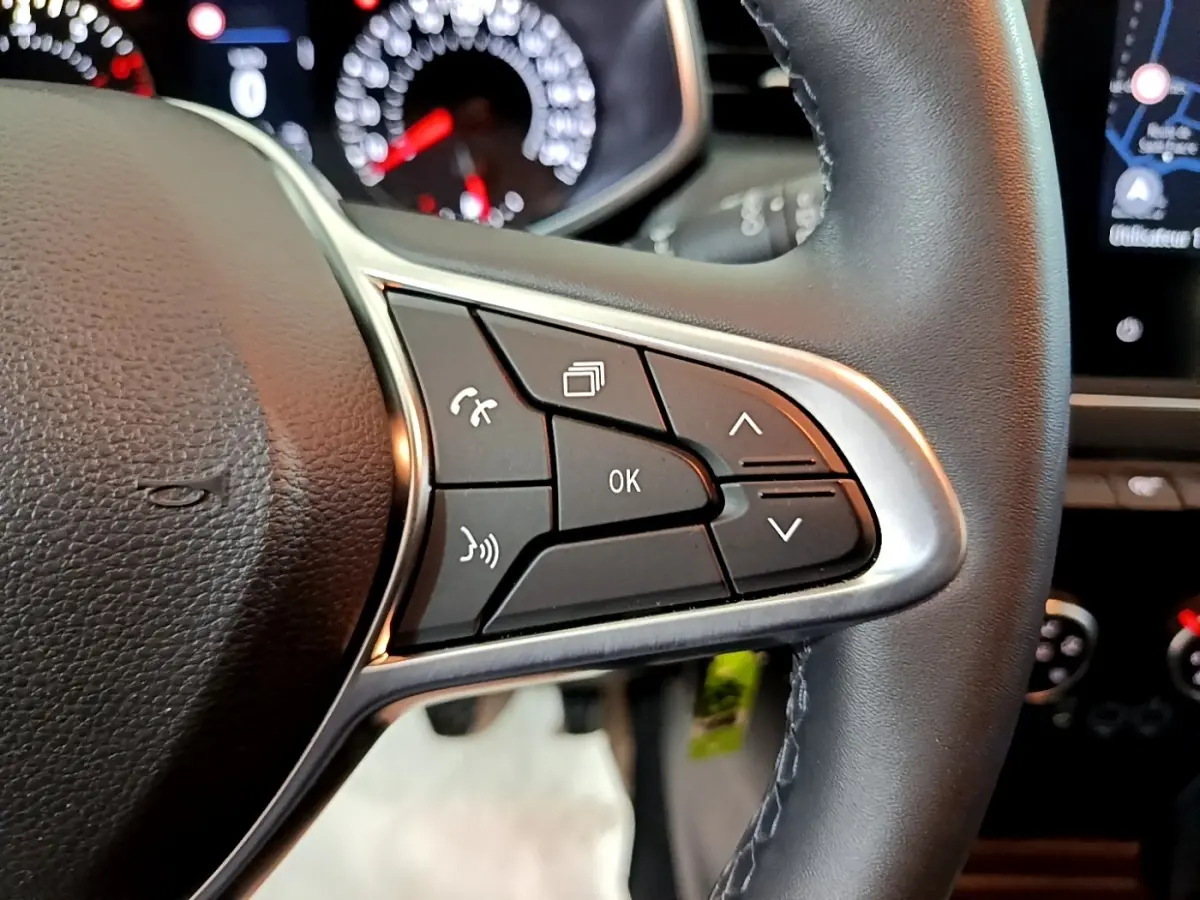 Gros plan sur les commandes multifonctions du volant cuir noir de la Renault Clio Business blanche, tableau de bord en arrière-plan.