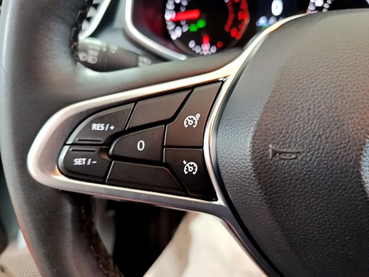 Gros plan sur les commandes de régulateur de vitesse au volant cuir noir de la Renault Clio Business blanche de 2021.