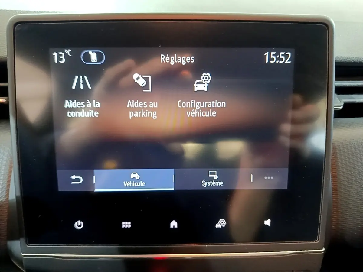 Écran tactile central du tableau de bord de la Renault Clio Business blanc, affichant les réglages d’aide à la conduite et parking.