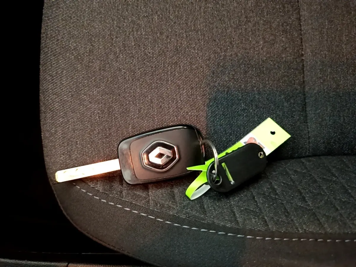 Clé de voiture Renault posée sur un siège avant en tissu noir avec surpiqûres visibles.
