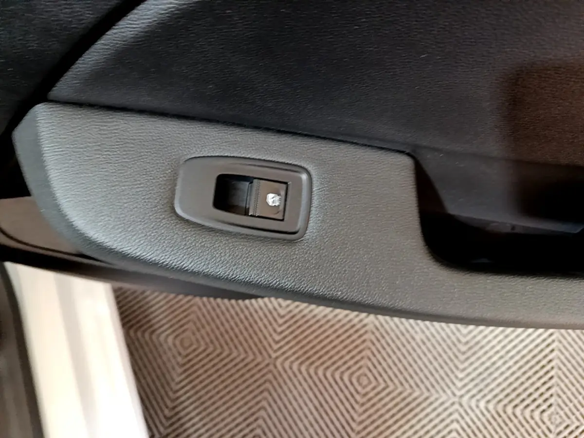 Gros plan sur la commande de verrouillage de porte noire dans l’intérieur côté gauche d’une Renault Clio Business blanche.