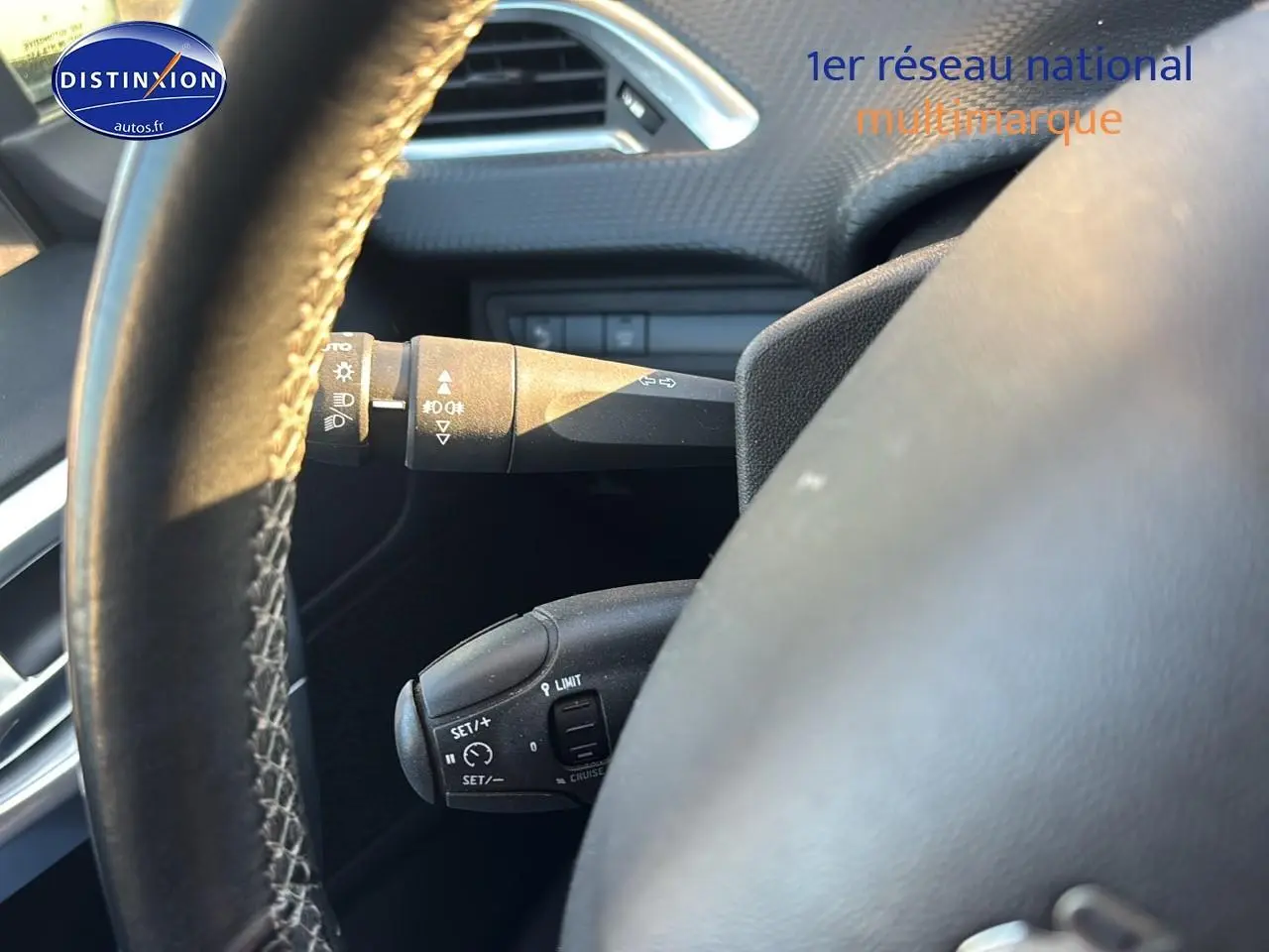 Gros plan sur le volant cuir multifonction du Peugeot 2008 gris clair, avec commandes de régulateur et clignotants visibles.