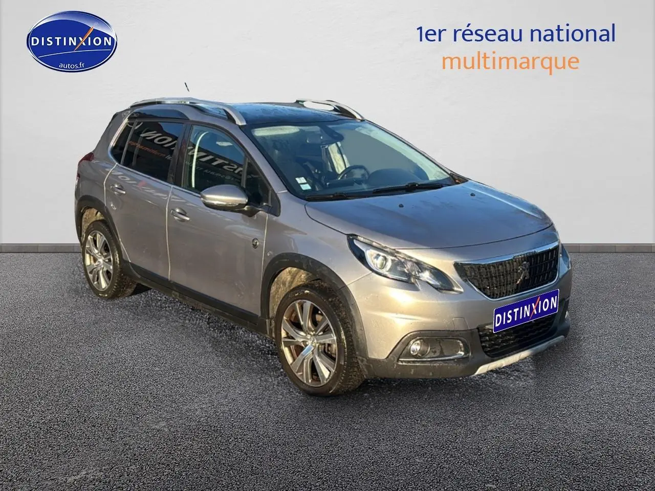 Peugeot 2008 gris clair en 3/4 avant droit avec barres de toit et jantes alu diamantées.
