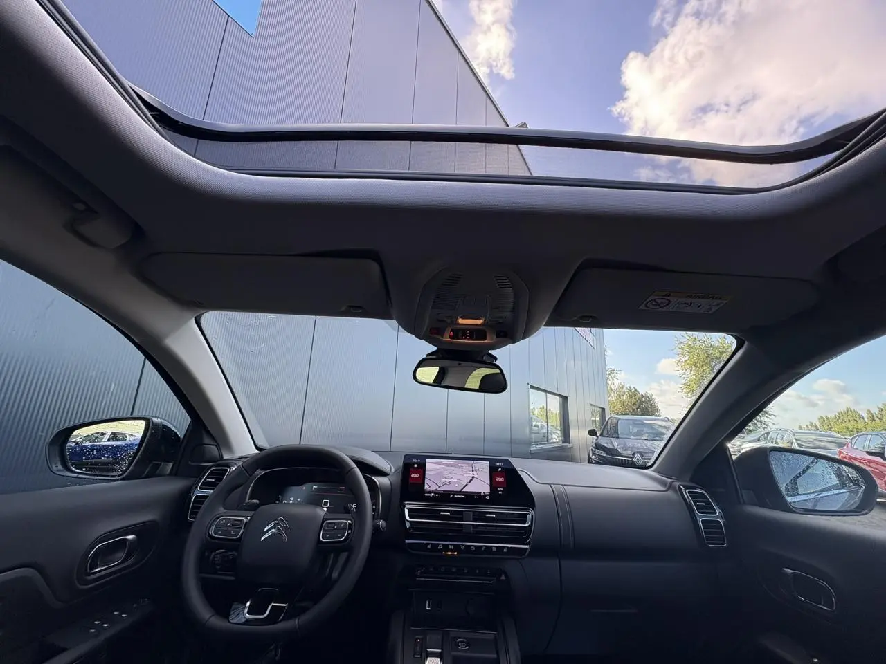 Vue intérieure avant du Citroën C5 Aircross 2025 avec toit ouvrant panoramique et tableau de bord noir moderne.