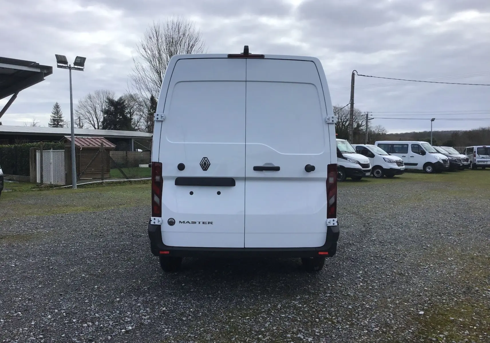 Vue arrière d’un Renault Master blanc L2H2 avec portes battantes fermées, sur un parking extérieur sous ciel nuageux.