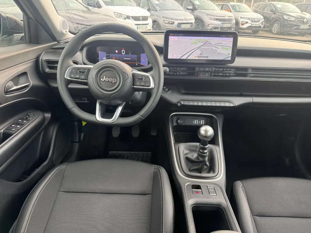 Vue intérieure avant du Jeep Avenger 2025 montrant le volant, la boîte manuelle et l'écran tactile de navigation.
