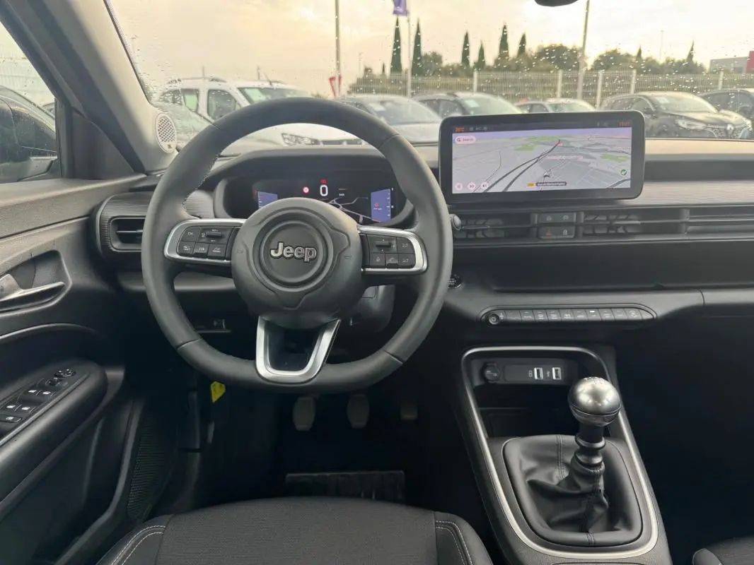 Vue intérieure avant du Jeep Avenger blanc 2025, volant multifonction, écran tactile et levier de vitesse manuel visibles.